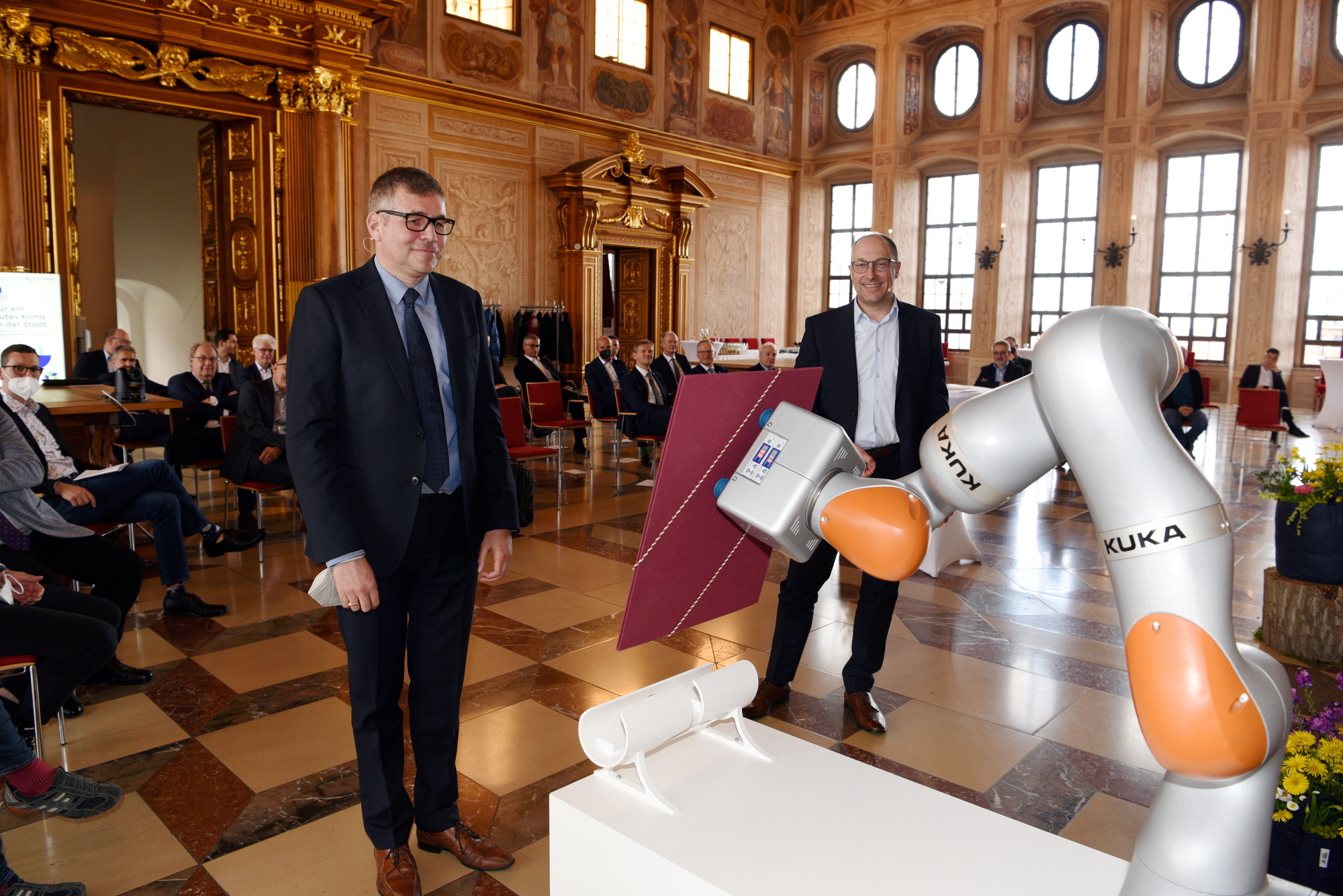 Übergabe des Klimapakts: Dr. Hübschle nahm die Vertragsmappe von einem Kuka-Roboter entgegen. Foto: Ruth Plössel/Stadt Augsburg