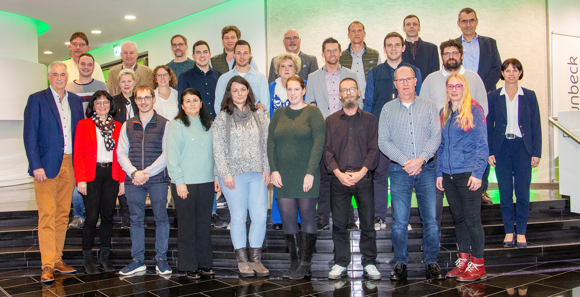 Eine Gruppe von Menschen steht zusammen vor einer grünen Wand.
