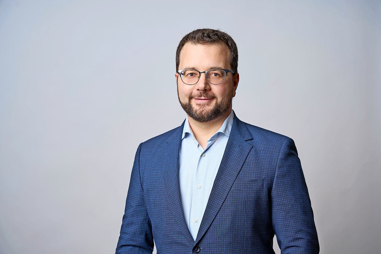 Ein Mann mit Brille und Anzug posiert vor einem grauen Hintergrund