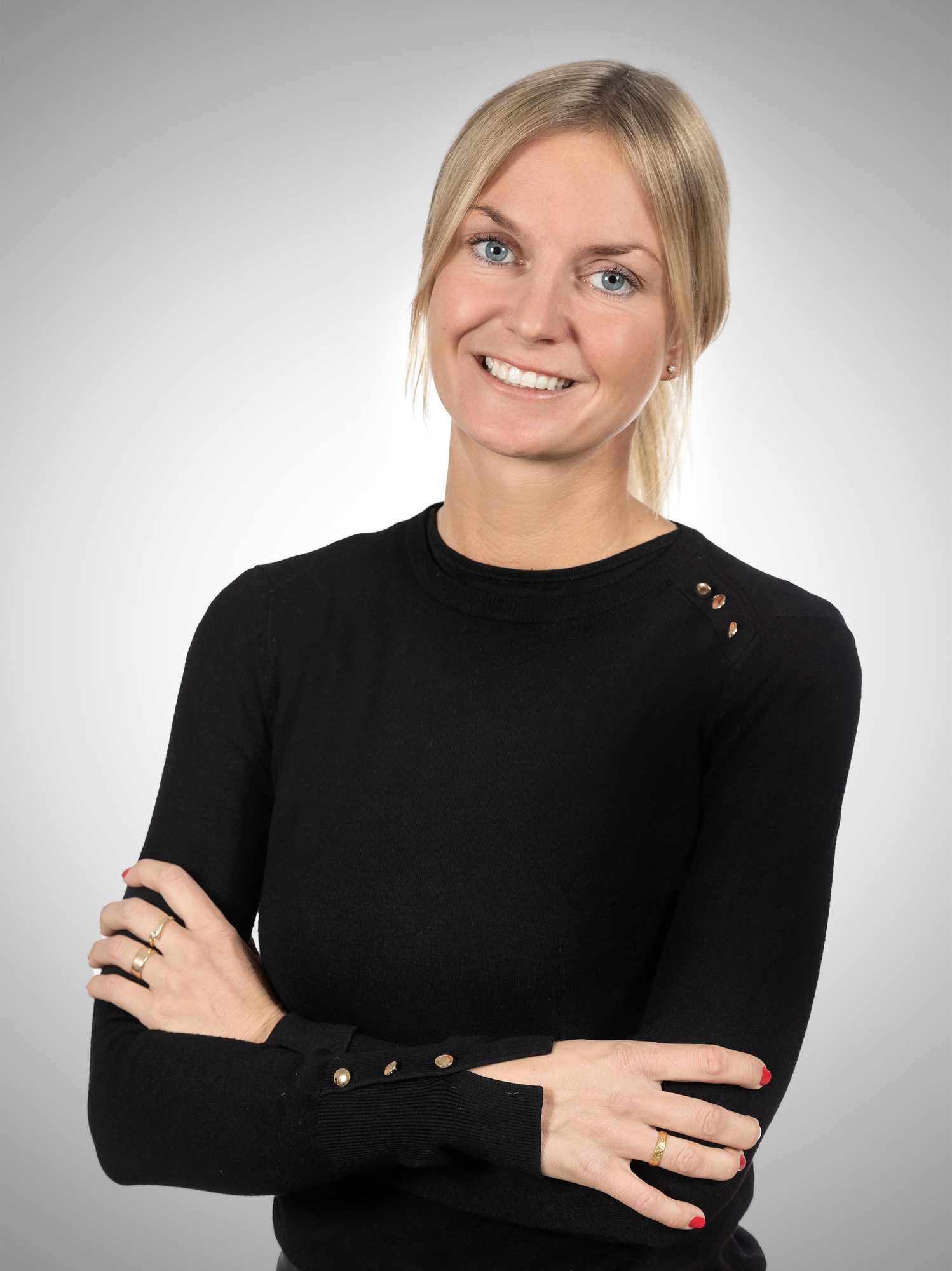 Eine blonde Frau mit schwarzem Oberteil präsentiert sich professionell vor einem weißen Hintergrund.