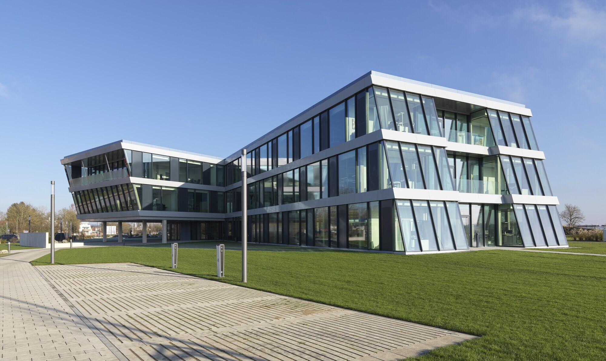Zeitgenössisches Bürogebäude mit transparenten Glaswänden, umgeben von grünem Rasen,