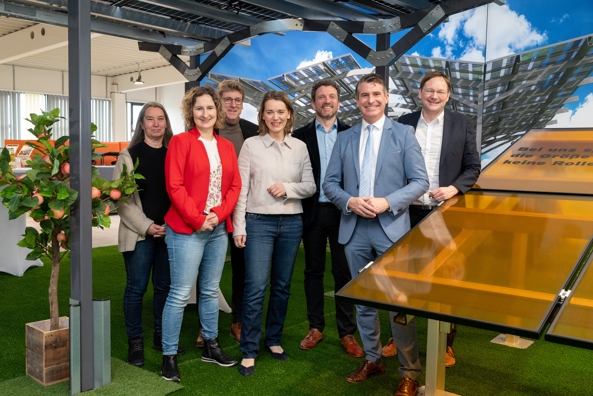 Eine Gruppe von sieben Personen steht neben einem Solarpanel