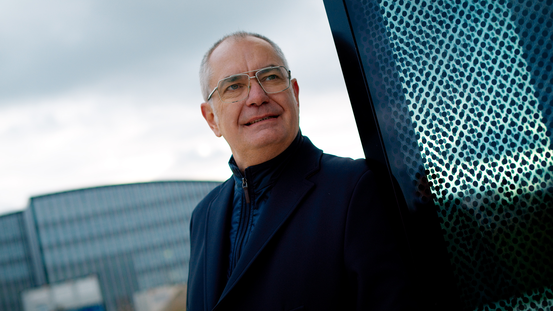 Michael Wörle lehnt sich an eine Glasfront und blickt nachdenklich in die Ferne.