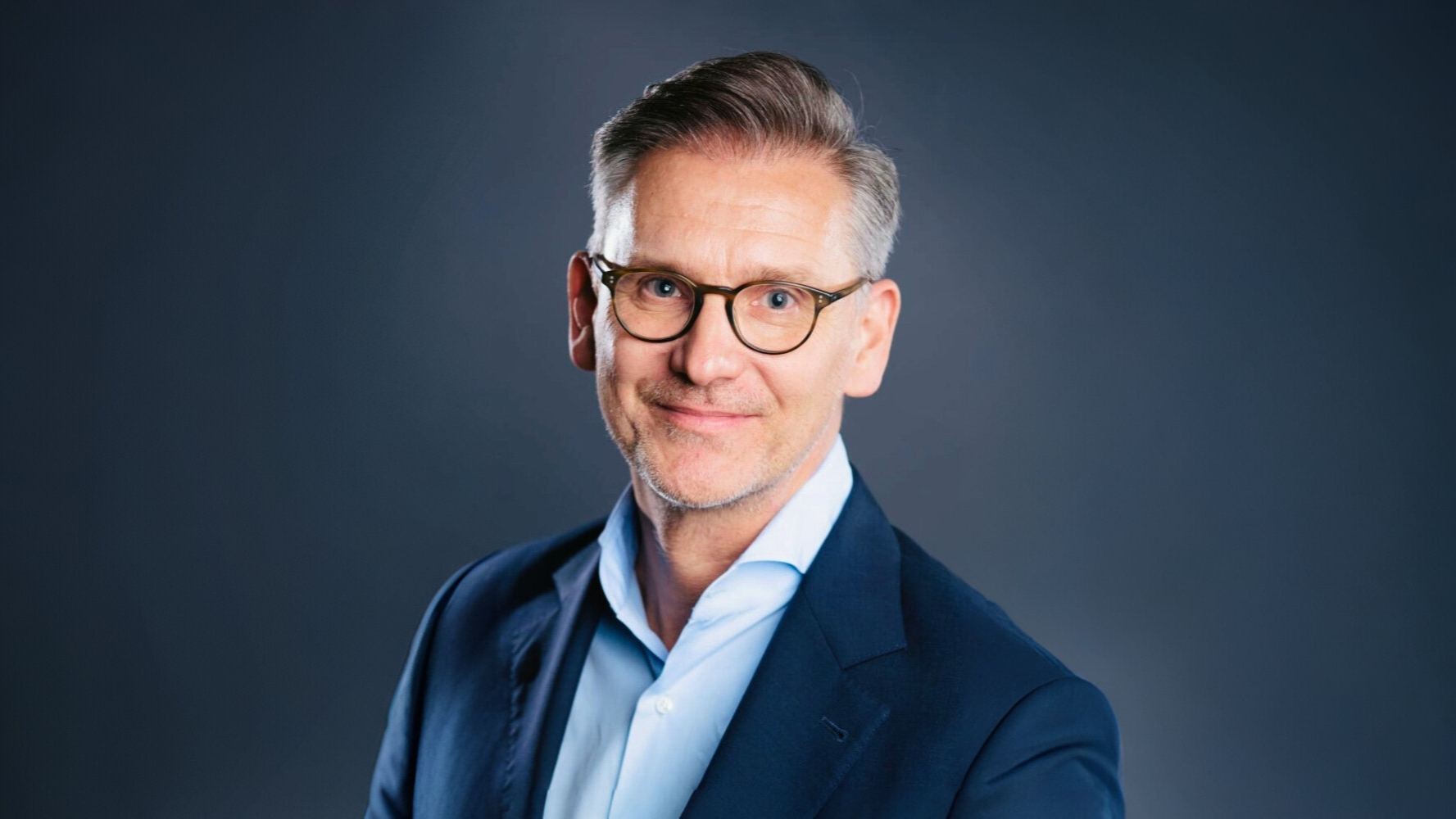 Felix Kovac hat einen dunkelblauen Anzug an und blickt lächelnd in die Kamera
