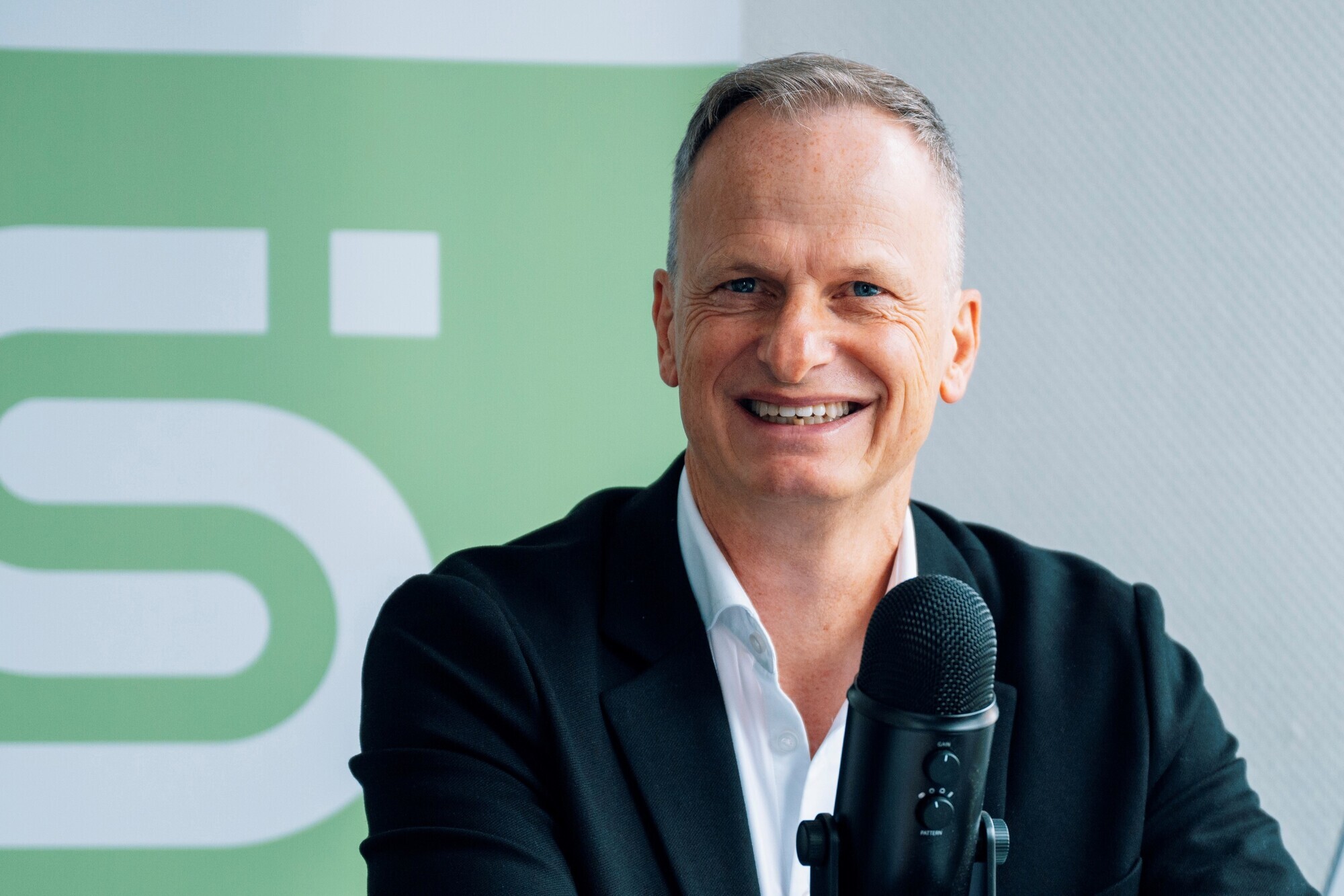 Oliver Dümpe sitzt an einem Tisch vor einem Mikrofon und lächelt in die Kamera