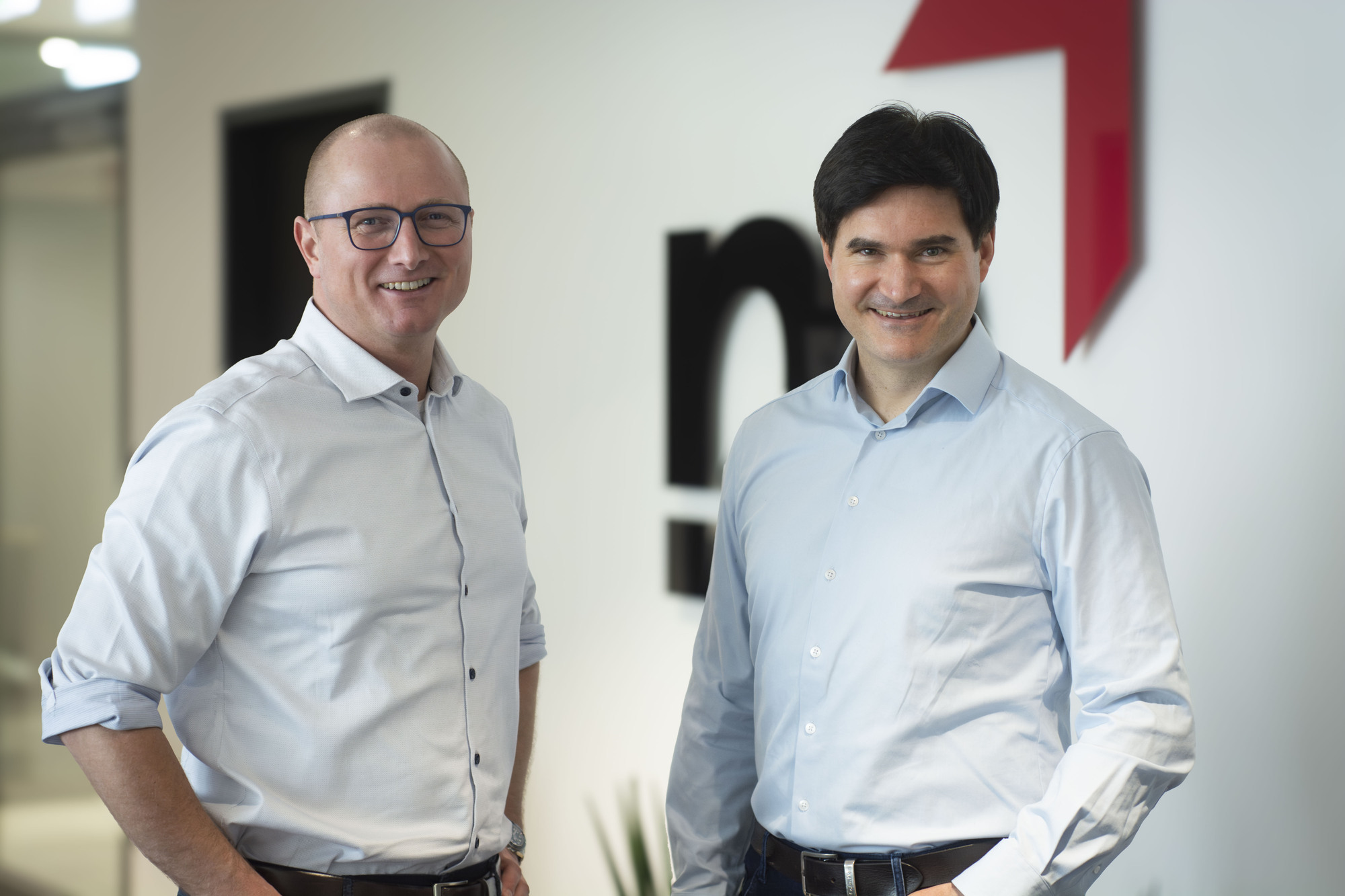 Dr. Thomas Eisenbarth und Fabian Rimpl lächen in die Kamera. Sie stehen vor einer Wand mit dem Makandra-Logo.