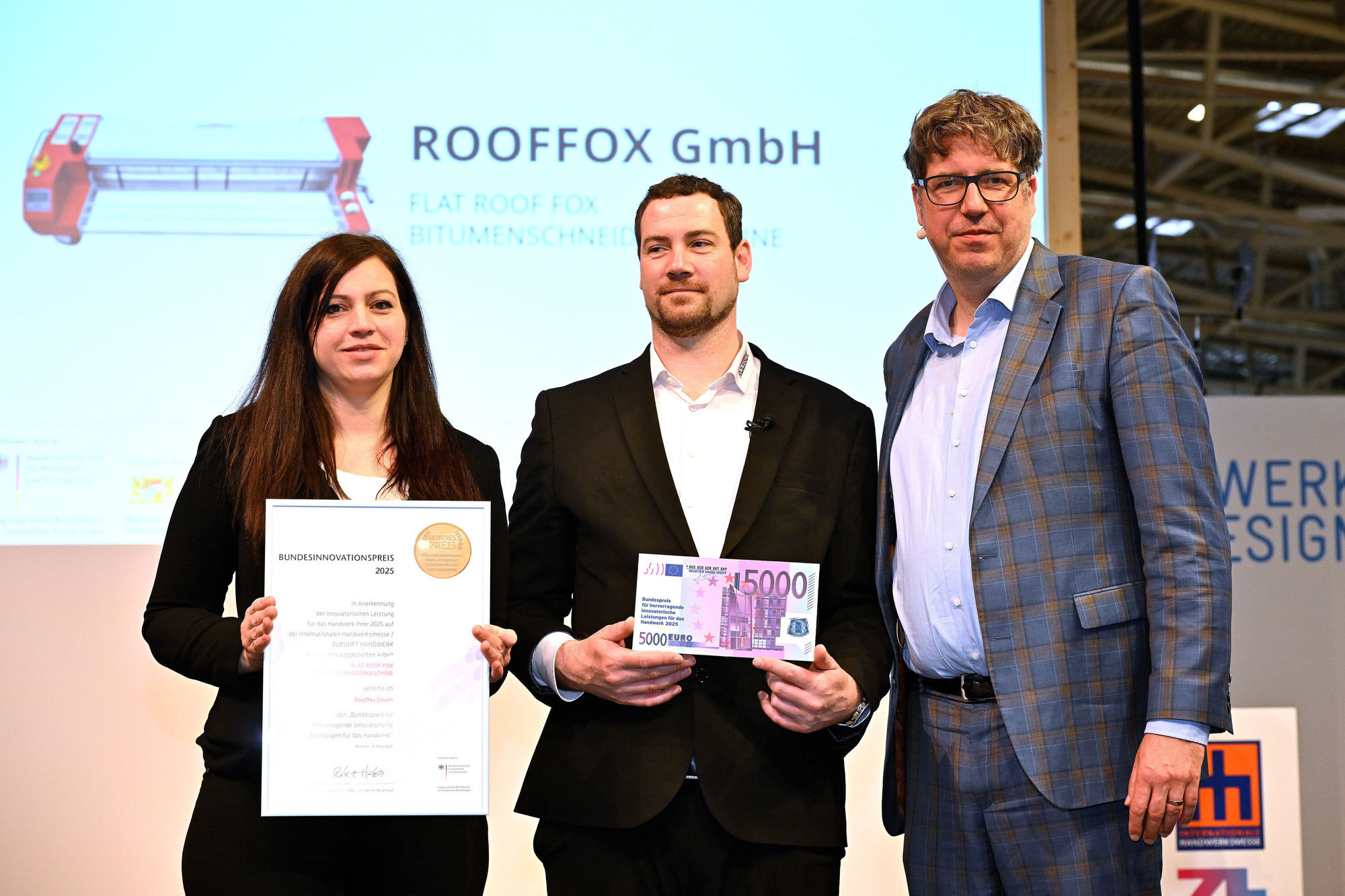Marlies Klinger hält die Urkunde des Bundespreises hoch, Tobias Büttgen einen symbolischen Preisgeldschein.