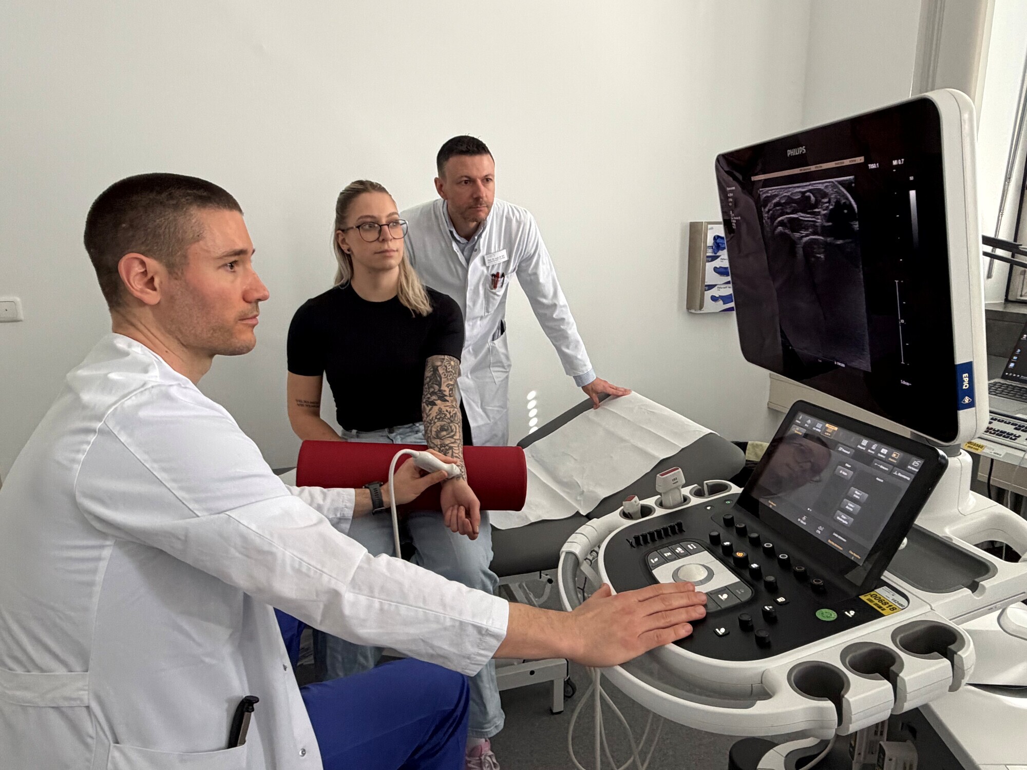 Dr. Daniel Rapp (links) und Prof. Michael Ertl (rechts) nehmen am Handgelenk der Medizinisch-Technischen Assistentin (MTA) Bianc